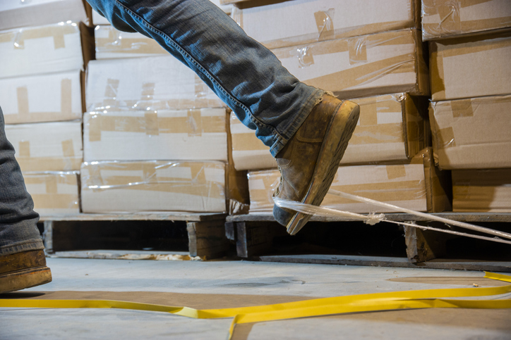 Warehouse worker's boot gets snagged on debris laying on the floor.