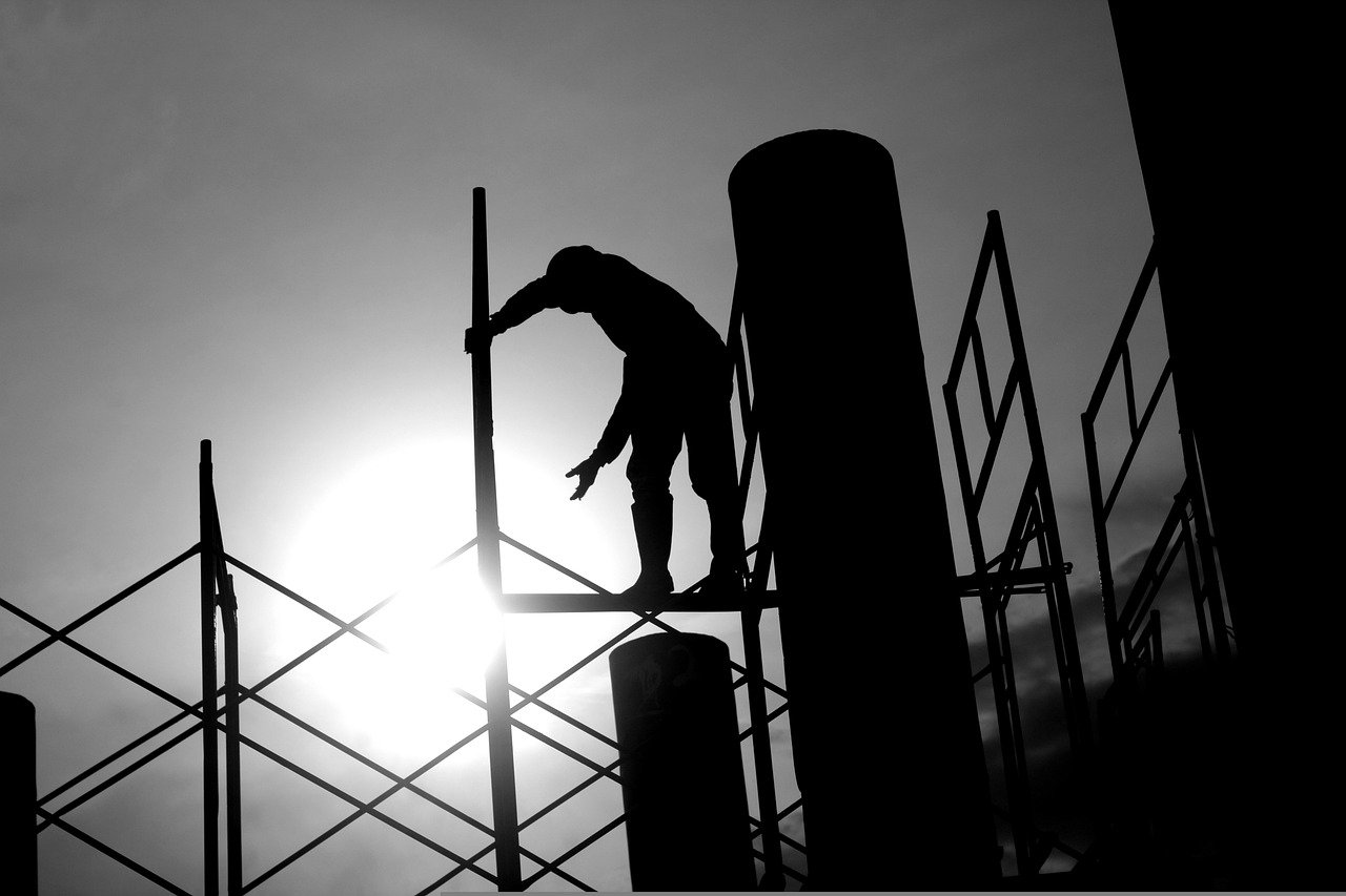 silhouette of a construction worker high above the ground on a steel beam.