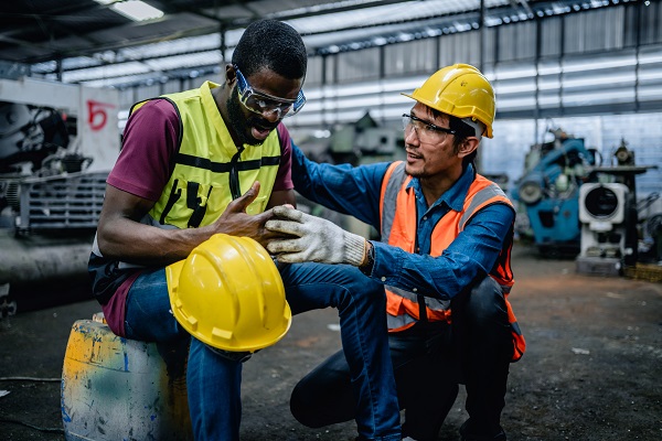 A factory worker with a finger injury is helped by a co-worker.