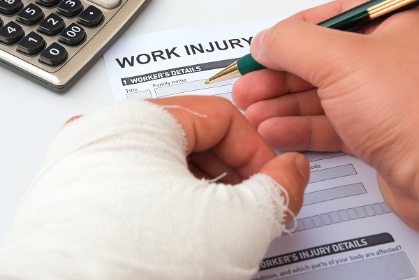 Injured worker with a bandaged hand uses a pen to fill out a work injury claim form.